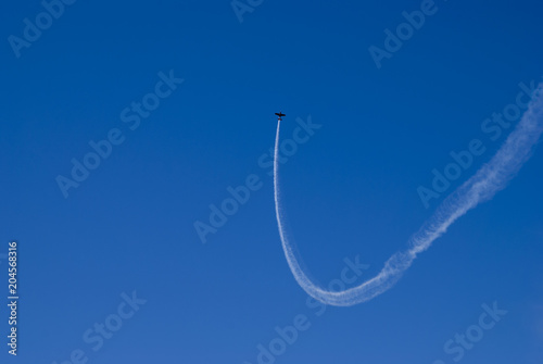 Black airplane flies up with  a white smoke in blue sky