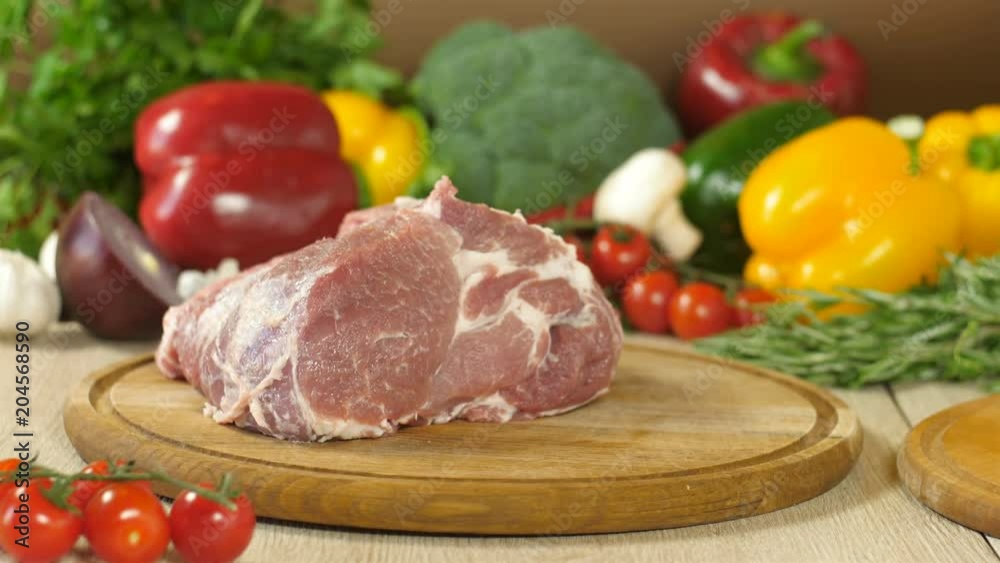 Chef throws a piece of raw juicy meat on a round wooden board, in the background vegetables greens, broccoli, red pepper, red onion, garlic, cherry tomatoes, sprigs of rosemary and thyme, the Chef throws a piece of raw juicy meat on a round wooden board, in the background vegetables greens, broccoli, red pepper, red onion, garlic, cherry tomatoes, sprigs of rosemary and thyme, the