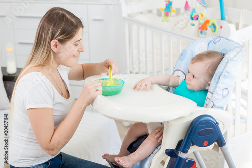 Portrait of smiling young mother feeding her baby in living room