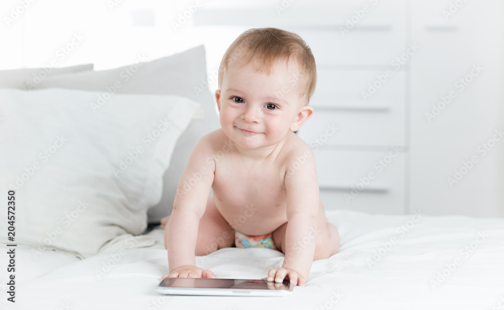 Portrait of smiling baby boy in diapers crawling towards digital tablet computer and looking in camera Portrait of smiling baby boy in diapers crawling towards digital tablet computer and looking in camera