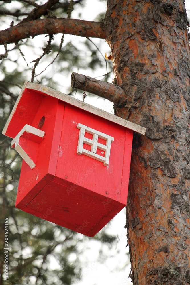 Wooden lodge for birds of red color on a tree trunk.