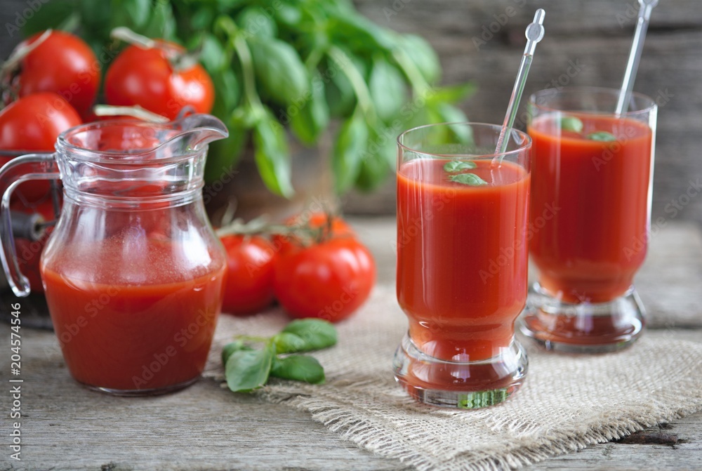 Tomato juice in glasses and tomato on wooden table on wooden background Tomato juice in glasses and tomato on wooden table on wooden background