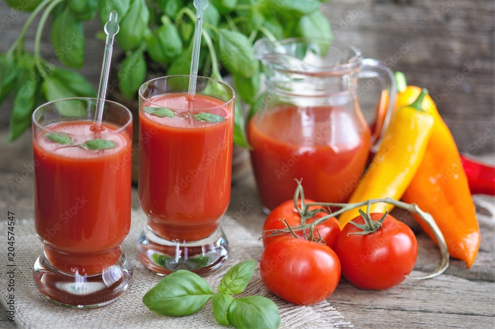 Tomato juice in glasses and tomato on wooden table on wooden background Tomato juice in glasses and tomato on wooden table on wooden background