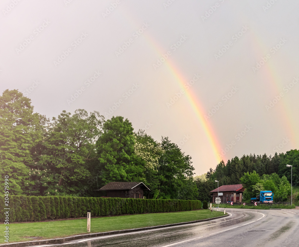 double rainbow over the road near village in forest