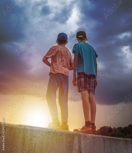 two boys brothers watching sunset under stormy sky