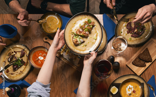 Table with food, top view. Flat-lay of friends hands eating and drinking together. People having party, gathering, celebrating together at wooden rustic table set with different wine and snacks