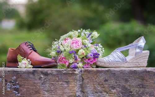 Brides wedding shoes with a bouquet with roses and other flowers on tha arm chair photo