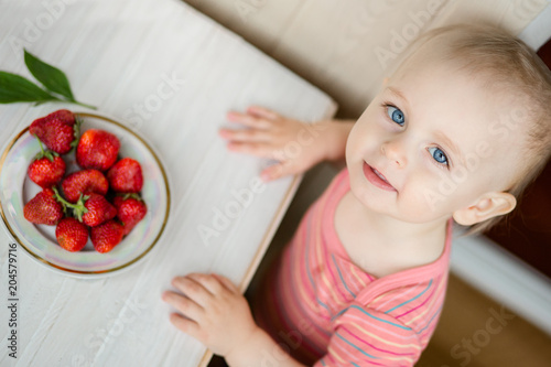 Hand of a child with a strawberry on a rustic background, a plate of strawberries.