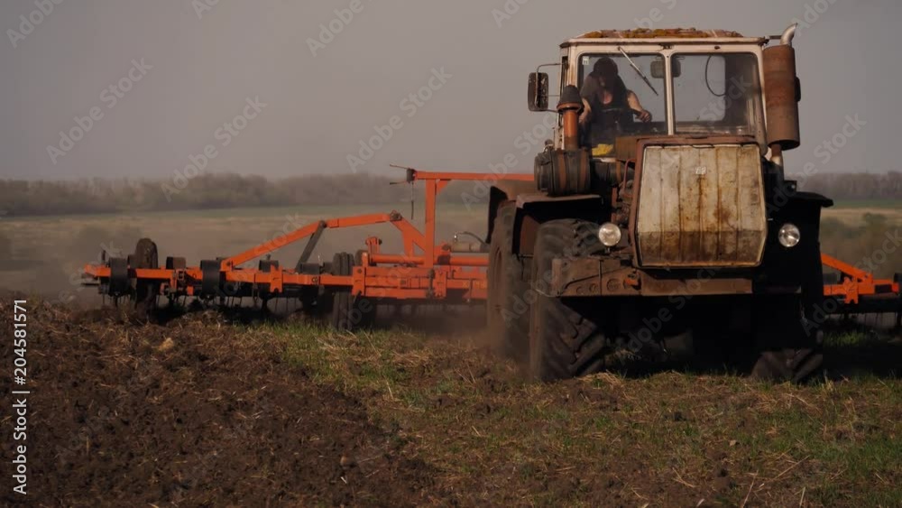 Tractor preparing land with seedbed cultivator as part of pre seeding activities of agricultural works at farmlands. Farmer in tractor preparing land with seedbed cultivator at sunset. Tractor preparing land with seedbed cultivator as part of pre seeding activities of agricultural works at farmlands. Farmer in tractor preparing land with seedbed cultivator at sunset.