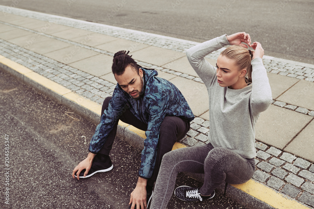 Young couple taking a break on a curb while jogging