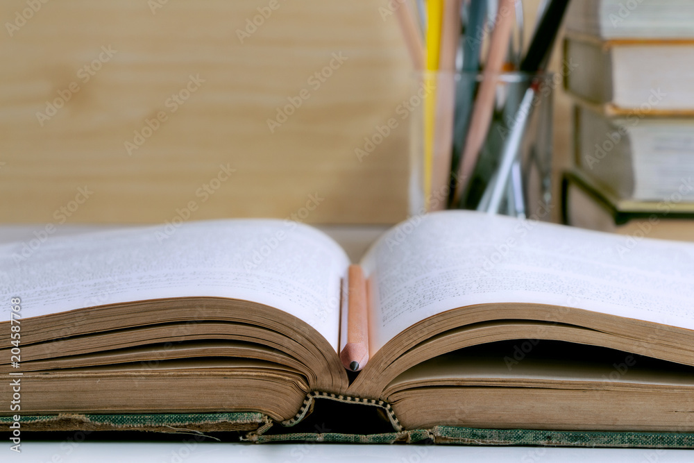 Open hardback and textbook stacked on the table background. Open hardback and textbook stacked on the table background.