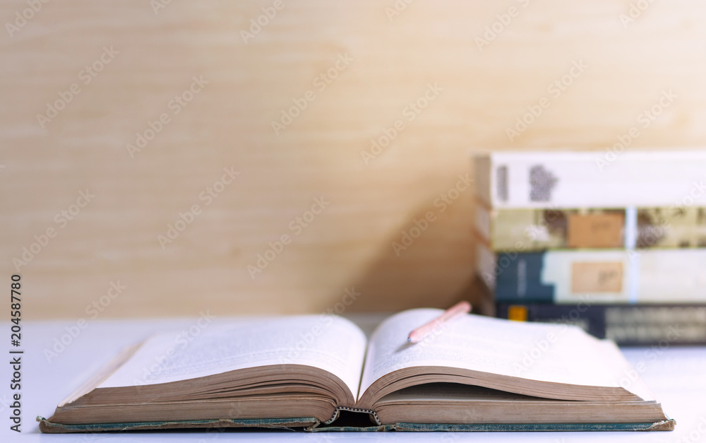 Open hardback and textbook stacked on the table on brown wall background. Open hardback and textbook stacked on the table on brown wall background.