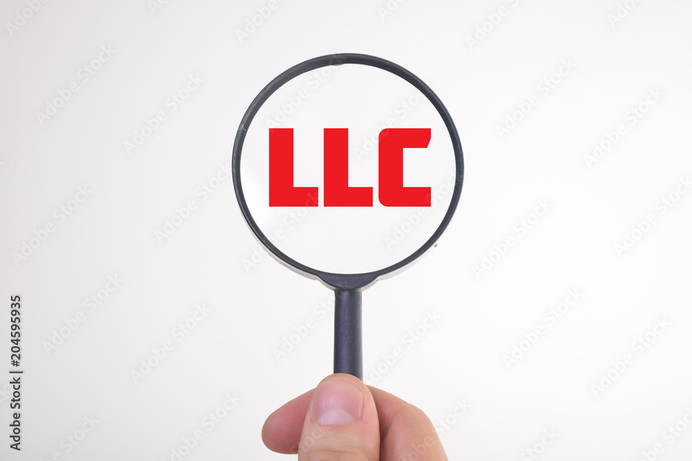 Businessman looking at a magnifying glass word:LLC Businessman looking at a magnifying glass word:LLC