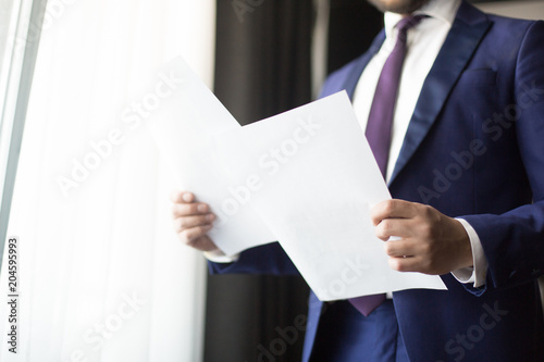 Financial papers or contracts in hands of economist or agent in suit standing by office window © pressmaster