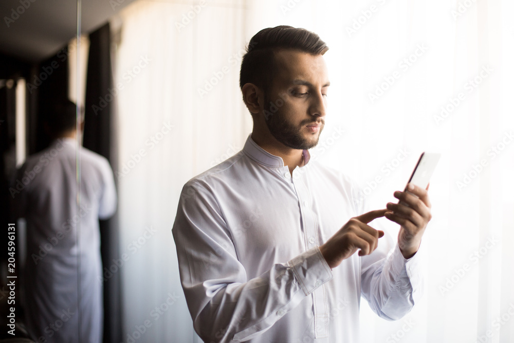 Serious young man with smartphone making voice record or reading message in white room Serious young man with smartphone making voice record or reading message in white room