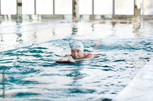 Active mature woman in swimwear swimming and exercising in water at lesiure