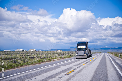Black classic big rig semi truck transporting commercial cargo on flat bed semi trailer in the flat straight road in Nevada © vit