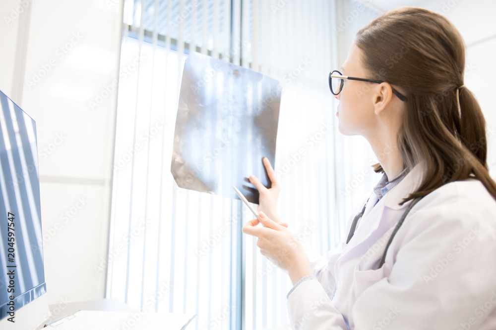 Young radiologist in uniform looking at x-ray image while working in hospital or clinics Young radiologist in uniform looking at x-ray image while working in hospital or clinics