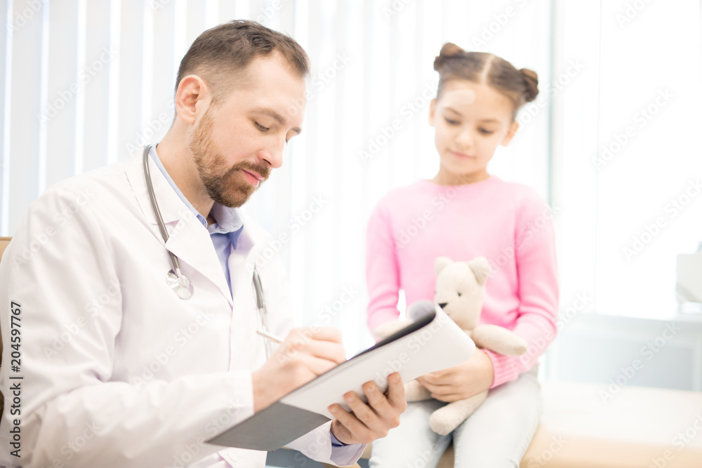 Young pediatrician writing down prescriptions for his little patient in modern clinics Young pediatrician writing down prescriptions for his little patient in modern clinics