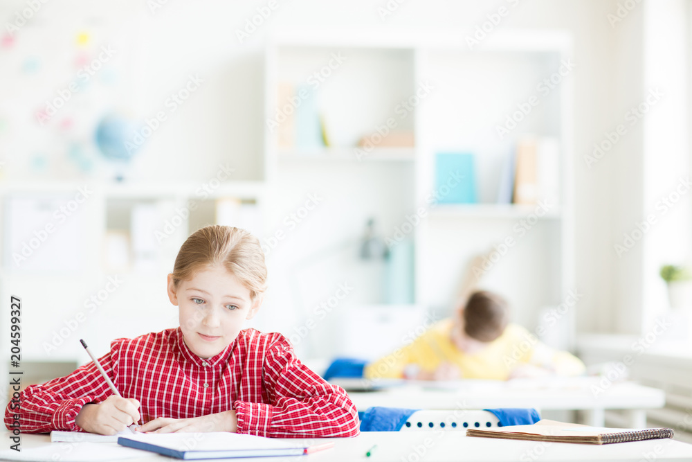 Diligent student of secondary school reading text in book and making notes in her copybook during individual work Diligent student of secondary school reading text in book and making notes in her copybook during individual work
