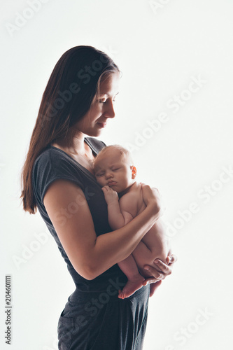 mother in gray t-shirt holds on the hands of his bare newborn baby. Woman with a baby in her arms. The girl kisses the child on the forehead
