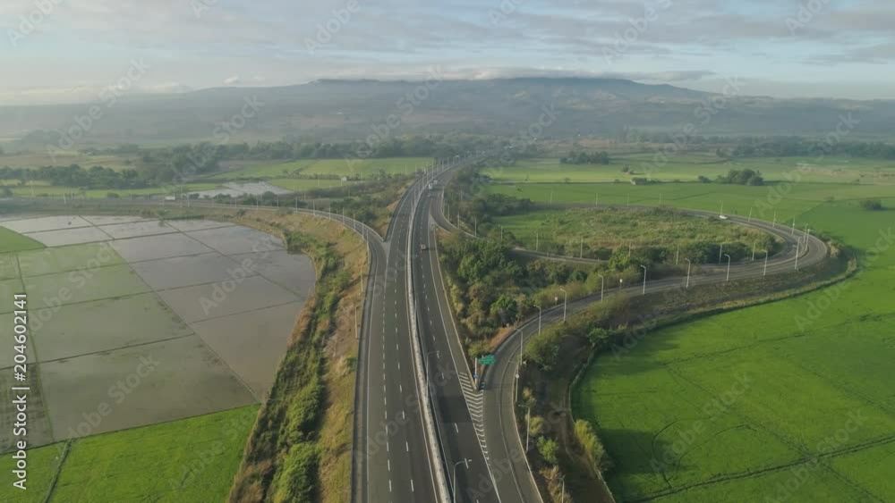 Aerial view highway with cars among farmer fields, rice terraces on background of mountains. Philippines, Luzon. High speed highwayin the morning sunrise. Tropical landscape in Asia. Aerial view highway with cars among farmer fields, rice terraces on background of mountains. Philippines, Luzon. High speed highwayin the morning sunrise. Tropical landscape in Asia.