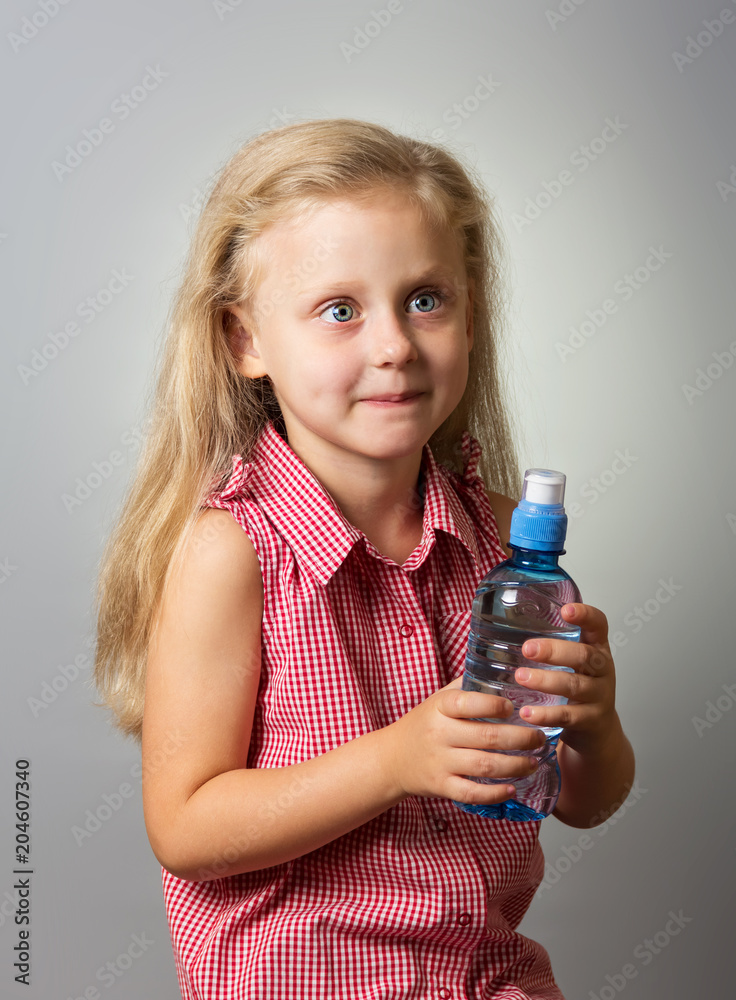 Adorable little girl with long hair holding a bottle of water on gray Adorable little girl with long hair holding a bottle of water on gray