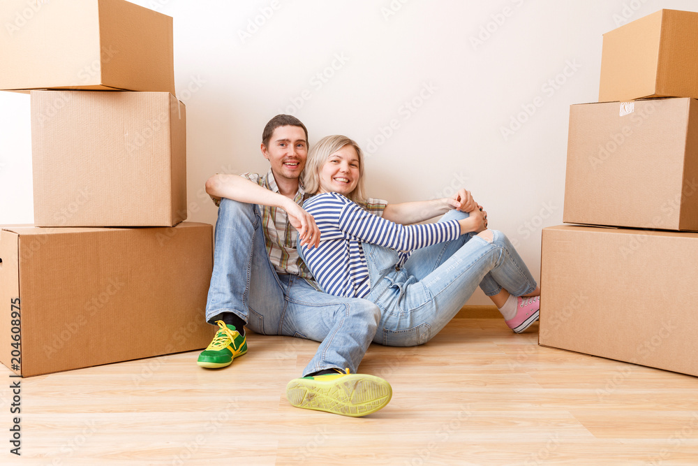 Photo of young couple sitting on floor among cardboard boxes Photo of young couple sitting on floor among cardboard boxes