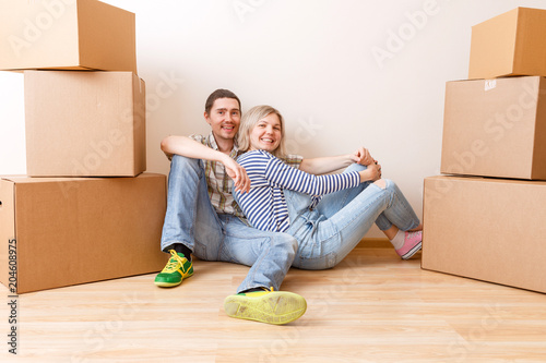 Photo of young couple sitting on floor among cardboard boxes