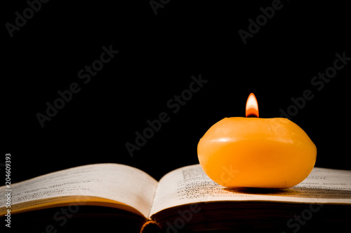 A lit candle standing on an open book