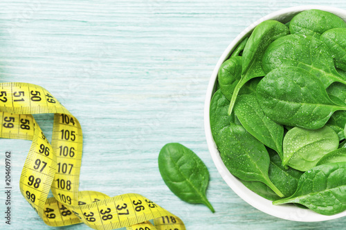 Tape measure and spinach leaves in bowl top view. Diet and healthy food concept.