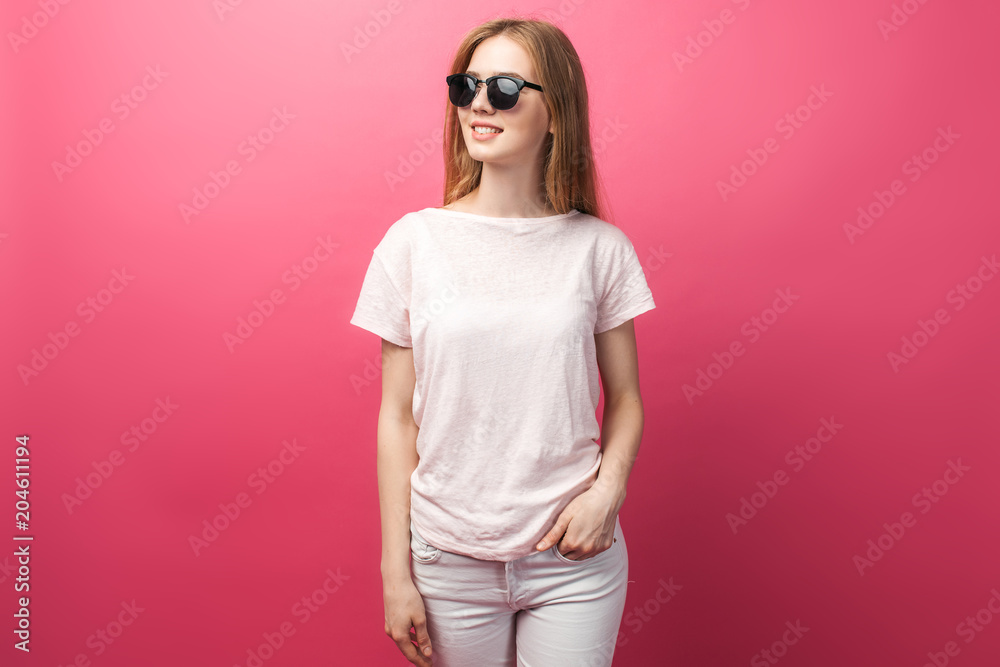 Beautiful young blonde girl in glasses standing on pink background wearing jeans, pink top smiling snow white smile, wearing black glasses and looking perfect promotional photo