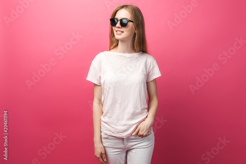 Beautiful young blonde girl in glasses standing on pink background wearing jeans, pink top smiling snow white smile, wearing black glasses and looking perfect promotional photo © Shopping King Louie