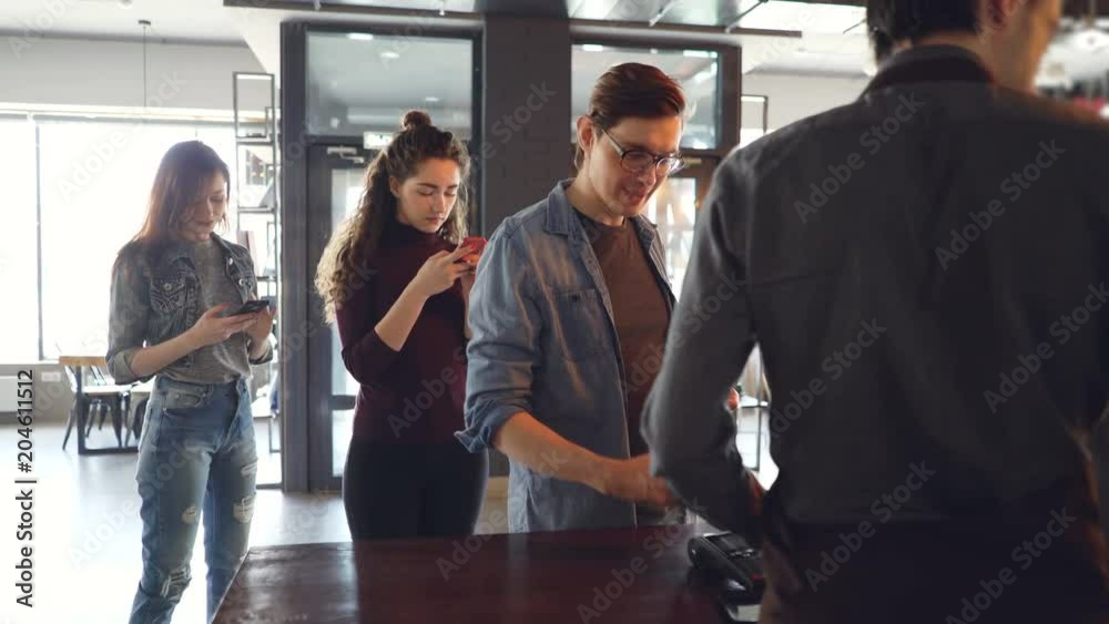 Cheerful customer in cafe is making payment with smartphone while queue of clients are waiting and using mobile phones. Takeaway drinks and modern banking concept.