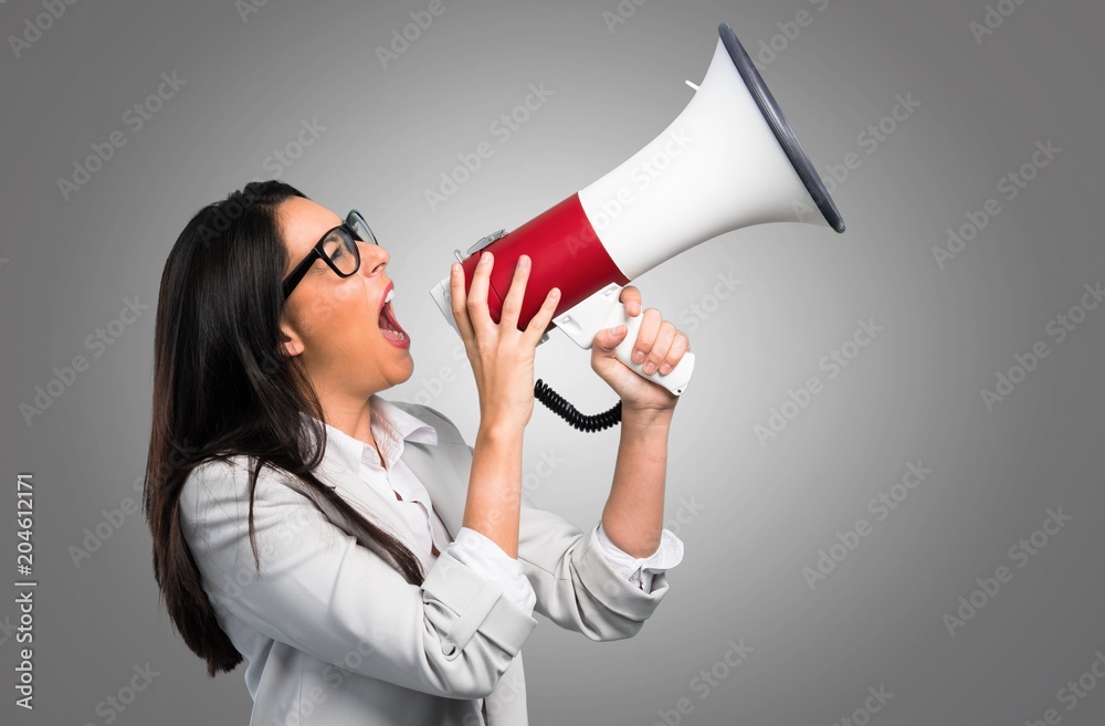 Pretty woman with glasses holding a megaphone on grey background Pretty woman with glasses holding a megaphone on grey background