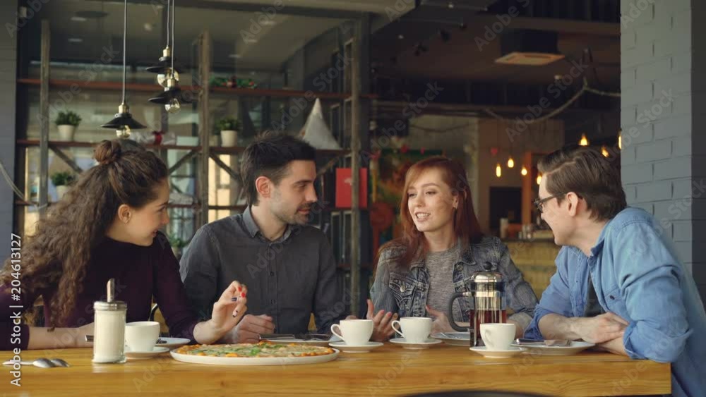 Cheerful attractive young lady is telling funny story to her friends at lunch in cafe, people are laughing and discussing it. Communication and eating out concept.