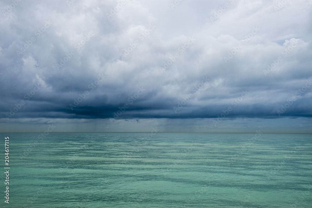 Calm tropical turquoise sea under darkening storm storm clouds on the horizon