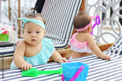 Cute twin baby in swimsuit on sun loungers.