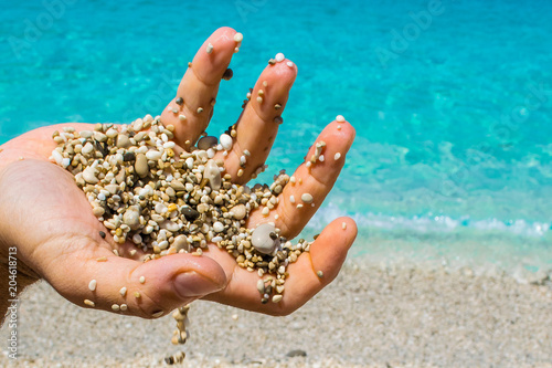 A man is playing with the sand and pebbles of the beach with his hand