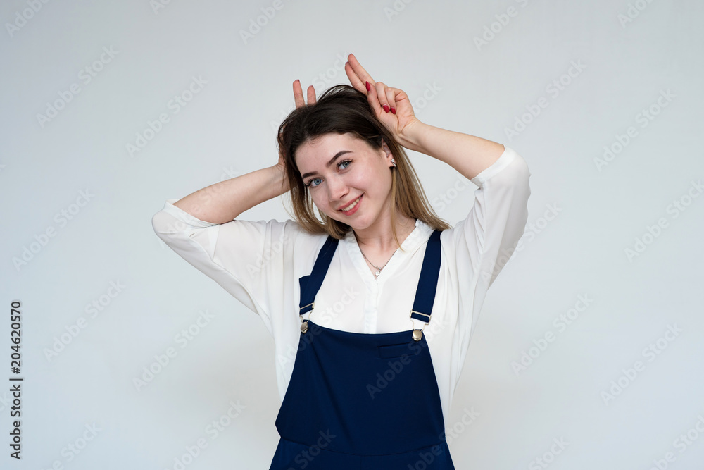 Portrait of a young beautiful girl on a white background with a smiling showing horns on the camera. Portrait of a young beautiful girl on a white background with a smiling showing horns on the camera.