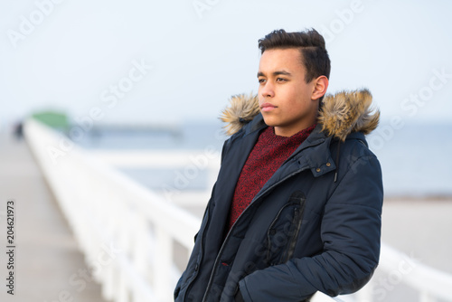  A young handsome teenage boy is dreaming away at the sea on a dock