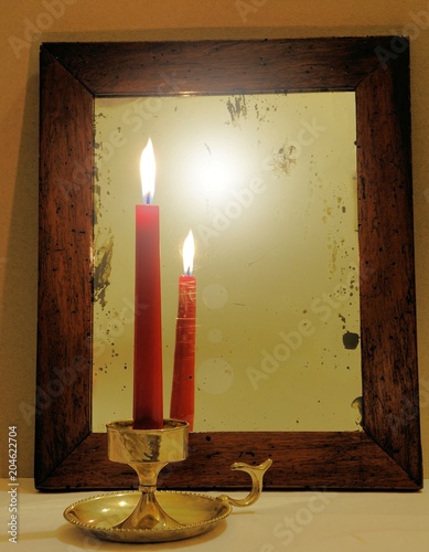 Red candle reflected in old mirror