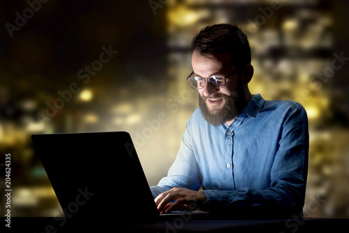 Young handsome businessman working late at night in the office with city lights in the background