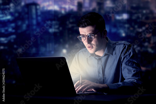 Young handsome businessman working late at night in the office with blue lights in the background