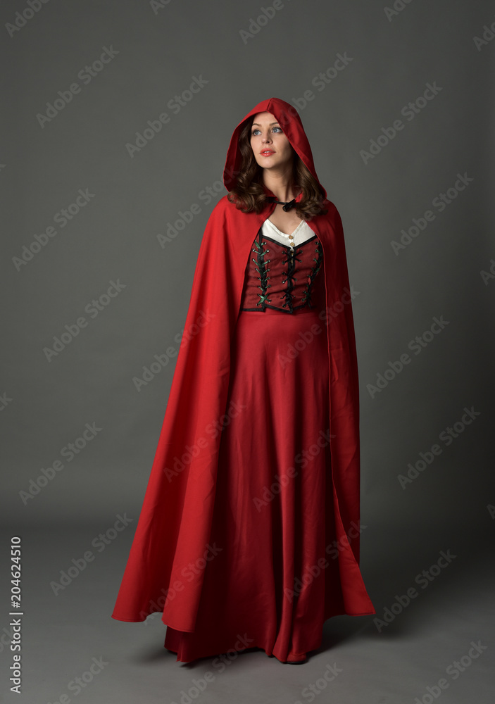 full length portrait of woman wearing red fantasy costume with cloak, standing pose on grey studio background. full length portrait of woman wearing red fantasy costume with cloak, standing pose on grey studio background.
