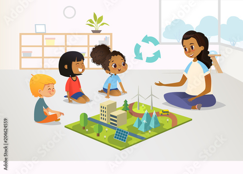 Smiling female kindergarten teacher and children sit on floor and explore toy model with renewable or sustainable energy systems, wind and solar eco friendly power stations. Vector illustration.