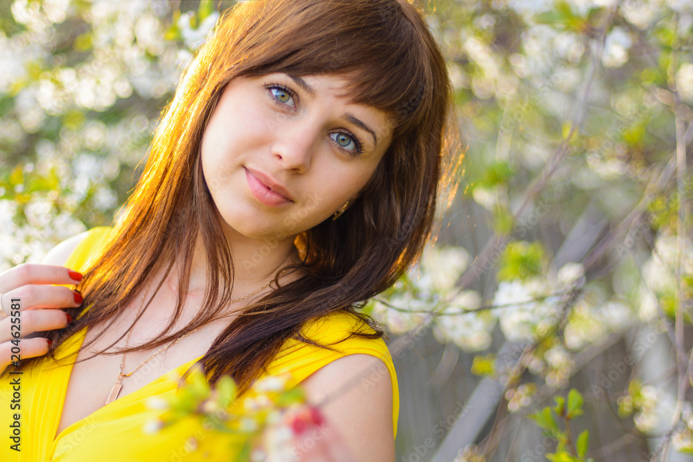 Naklejka premium young cute girl in yellow dress in spring on cherry blossom background