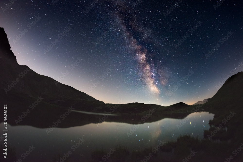Milky Way arch and starry sky reflected on lake at high altitude on the Alps. Fisheye scenic distortion and 180 degree view. Milky Way arch and starry sky reflected on lake at high altitude on the Alps. Fisheye scenic distortion and 180 degree view.