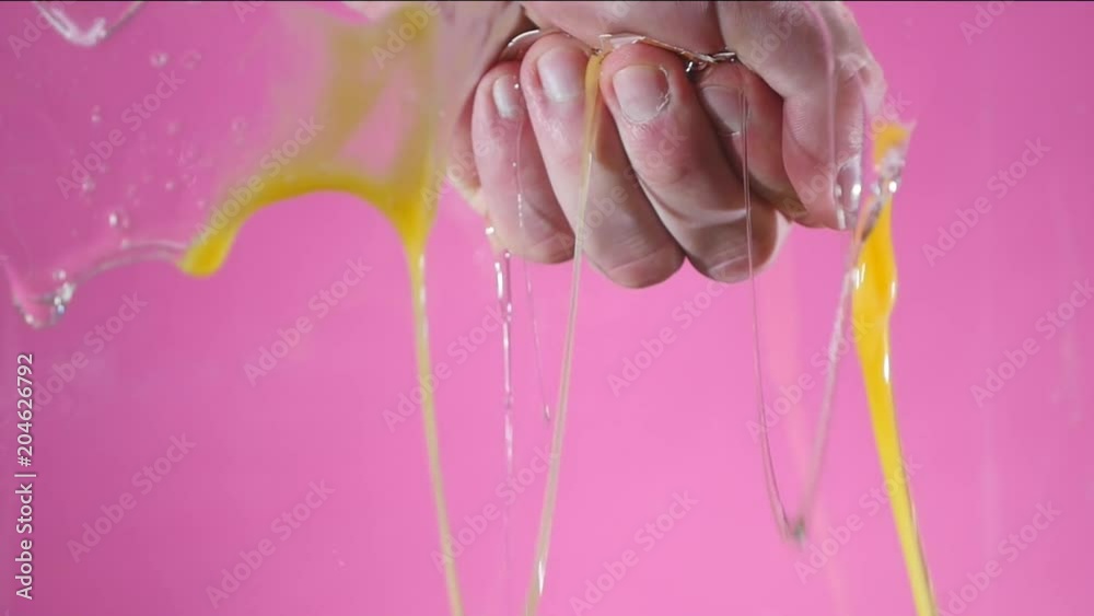 The hand compressed in a fist destroys an egg on a pink background