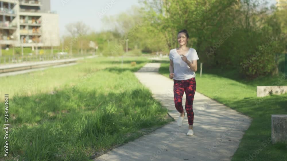 Young attractive female in sportswear smiling and running in park in the morning Young attractive female in sportswear smiling and running in park in the morning